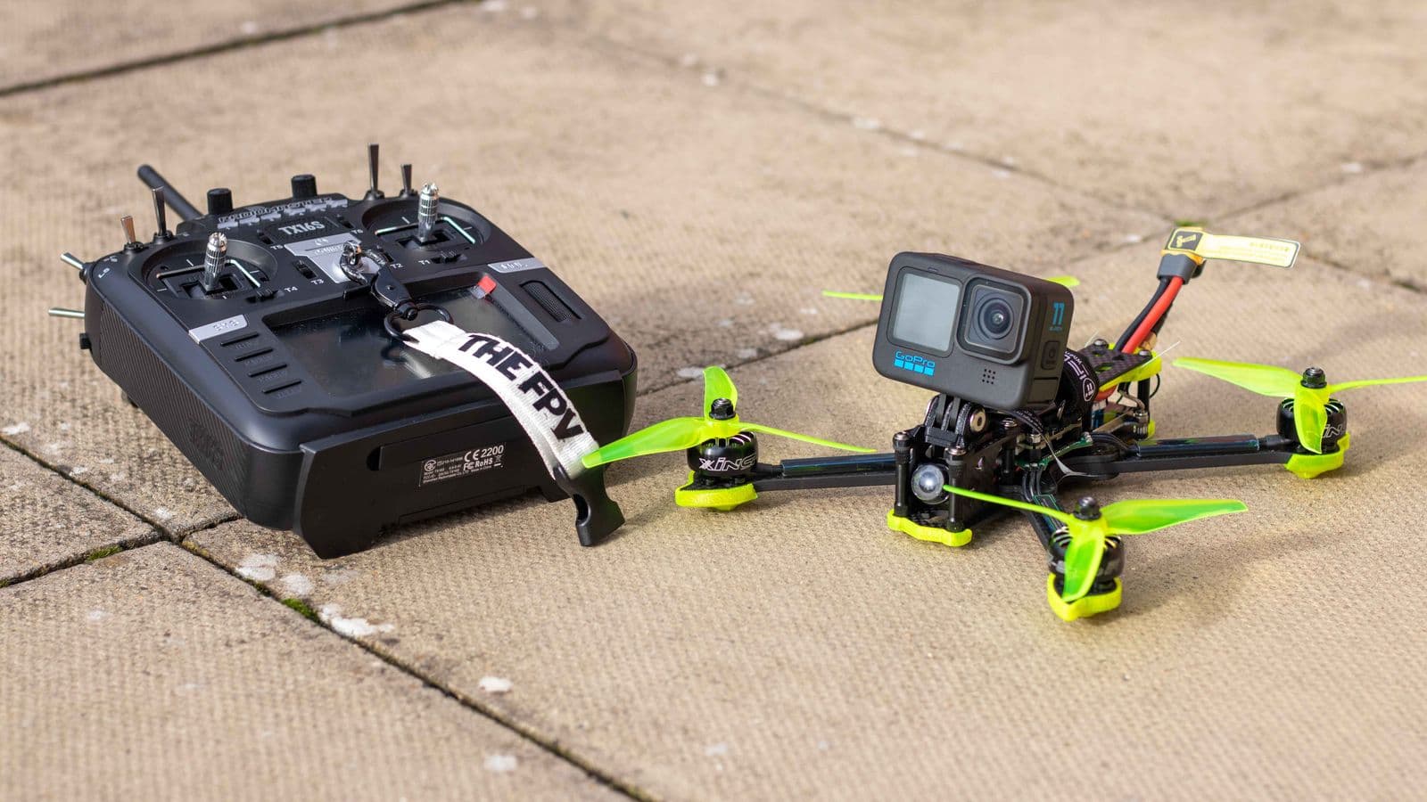 A compact FPV drone, radio controller and action camera on paving.