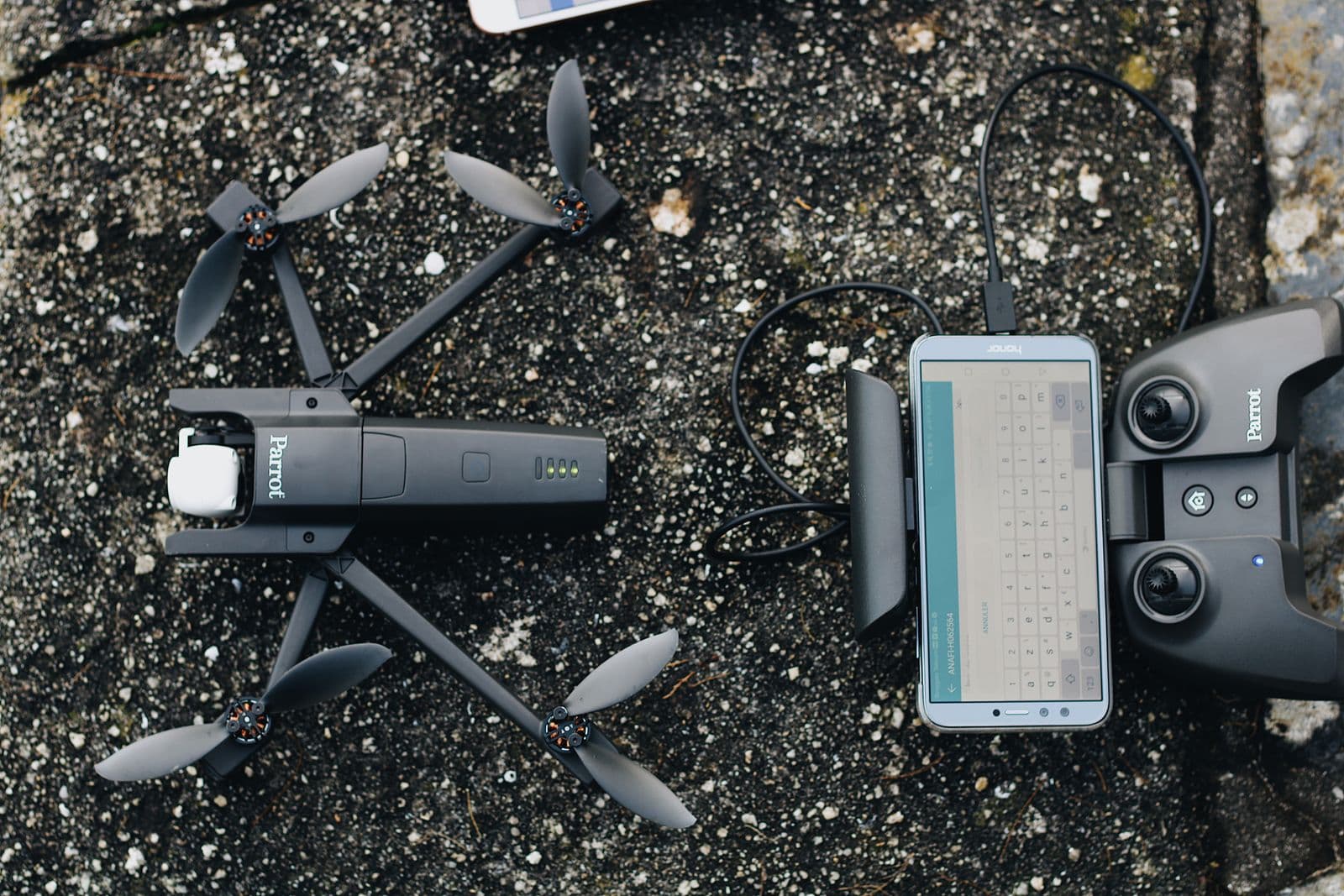 A folded drone, controller and phone laid out on textured ground before a flight.
